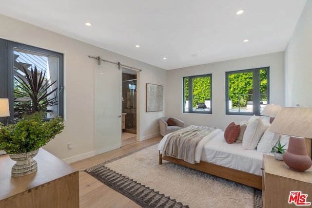 bedroom featuring light hardwood / wood-style floors, a barn door, and ensuite bathroom