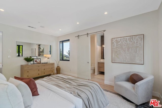 bedroom with light hardwood / wood-style floors, a barn door, and ensuite bathroom