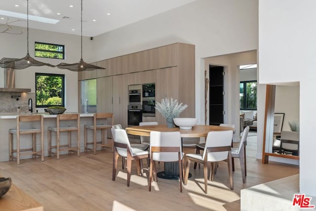 dining area featuring a high ceiling, a skylight, and light hardwood / wood-style flooring