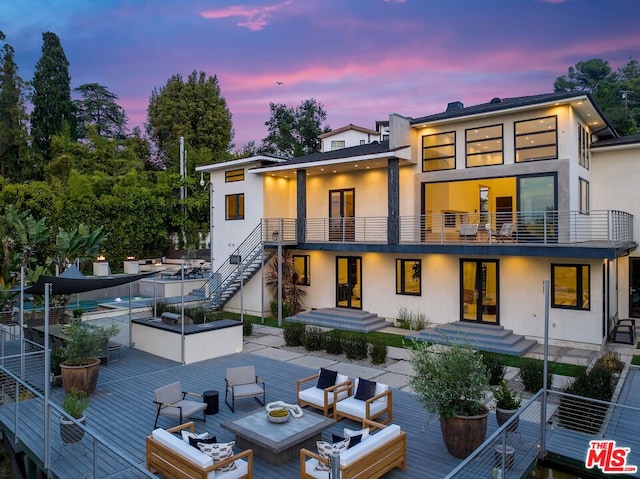 back house at dusk with outdoor lounge area and a balcony