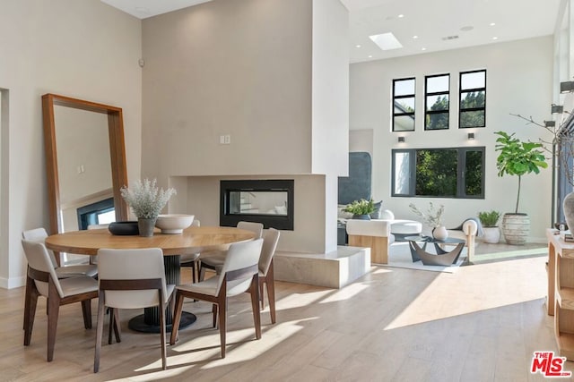 dining area with a multi sided fireplace, light hardwood / wood-style flooring, and a high ceiling