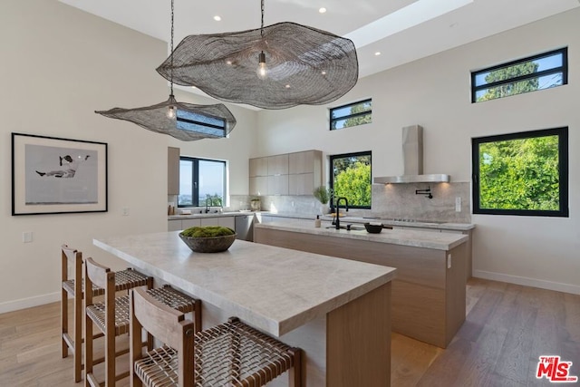 kitchen featuring wall chimney range hood, backsplash, light hardwood / wood-style floors, and a high ceiling