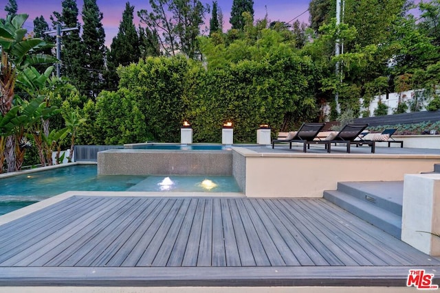 pool at dusk with pool water feature and an in ground hot tub