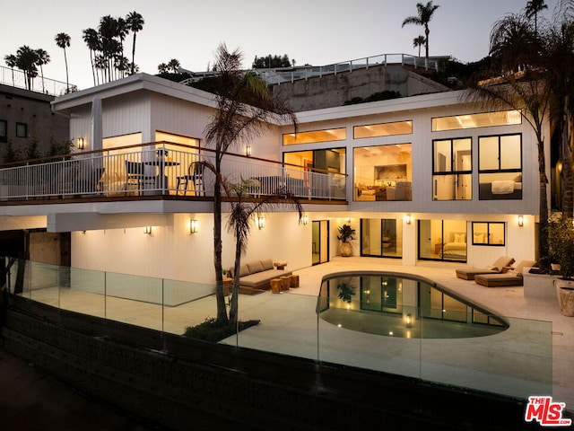 back house at dusk featuring a balcony and a patio area