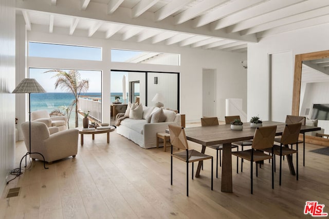 dining room with a water view, light hardwood / wood-style floors, and beamed ceiling