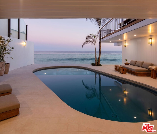 pool at dusk with a water view and outdoor lounge area