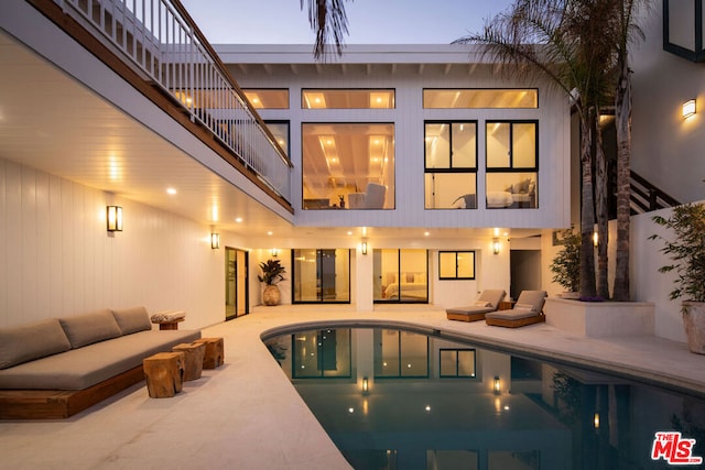 back house at dusk with an outdoor living space, a patio, and a balcony