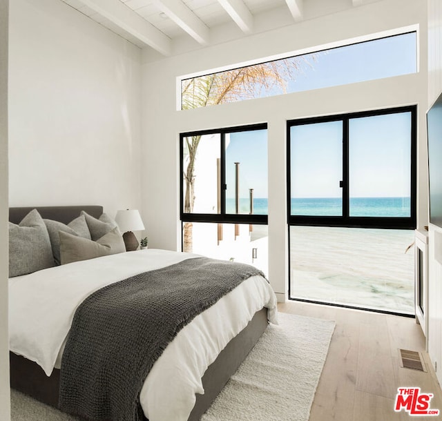 bedroom featuring beamed ceiling, a water view, and light wood-type flooring