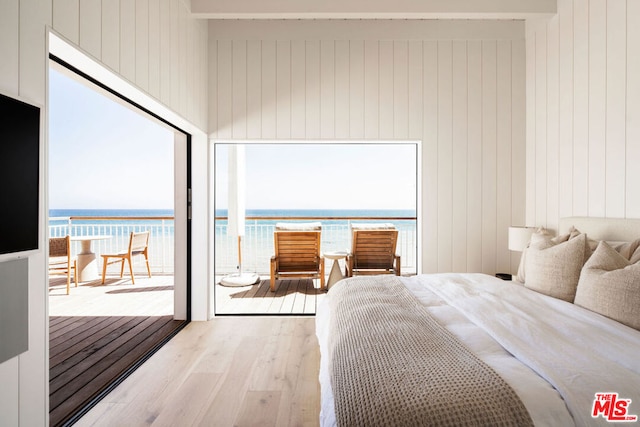 bedroom featuring light wood-type flooring, wooden walls, beamed ceiling, and a water view