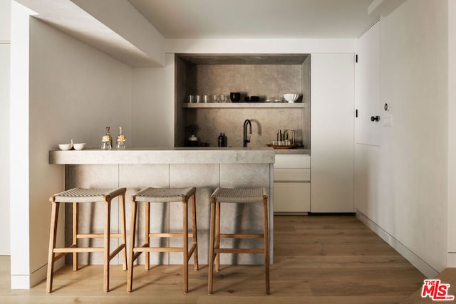 bar featuring sink, wood-type flooring, and white cabinets