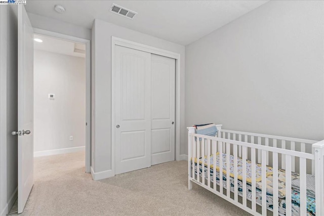 bedroom with a crib, light colored carpet, and a closet