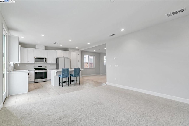 kitchen with appliances with stainless steel finishes, a breakfast bar area, white cabinets, a center island, and light colored carpet