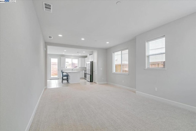 unfurnished living room featuring light carpet and a wealth of natural light