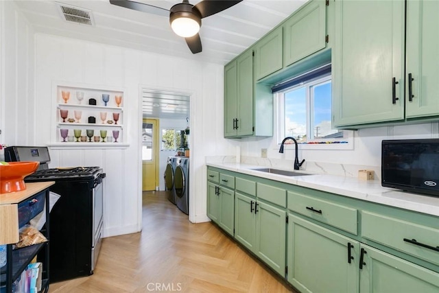 kitchen featuring sink, gas stove, green cabinetry, washer and dryer, and light parquet flooring