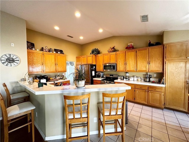 kitchen featuring vaulted ceiling, a breakfast bar area, light tile patterned floors, kitchen peninsula, and stainless steel appliances