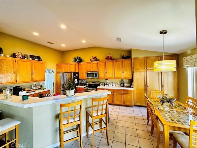 kitchen with light tile patterned flooring, hanging light fixtures, a kitchen breakfast bar, kitchen peninsula, and stainless steel appliances