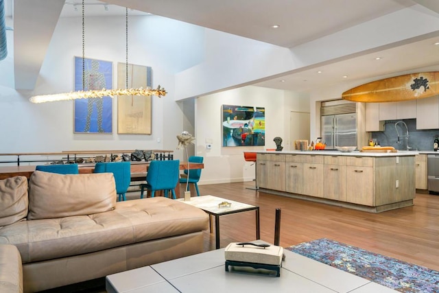 living room featuring an inviting chandelier, a towering ceiling, sink, and light hardwood / wood-style flooring