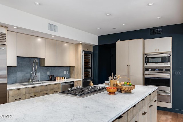 kitchen with sink, appliances with stainless steel finishes, light stone countertops, decorative backsplash, and beverage cooler