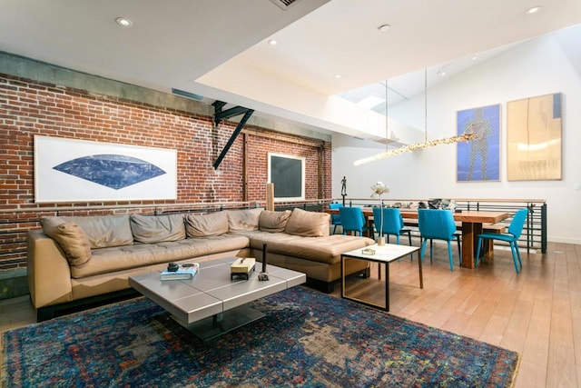 living room featuring lofted ceiling, wood-type flooring, and brick wall