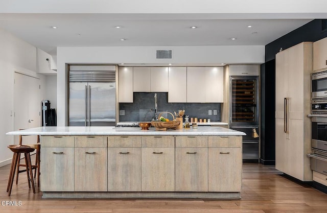 kitchen with a center island, built in appliances, backsplash, and light hardwood / wood-style flooring