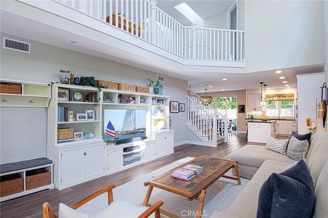 living room featuring a skylight, a towering ceiling, and dark wood-type flooring