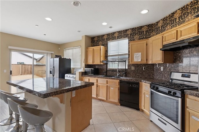 kitchen with appliances with stainless steel finishes, a kitchen bar, light brown cabinetry, and sink