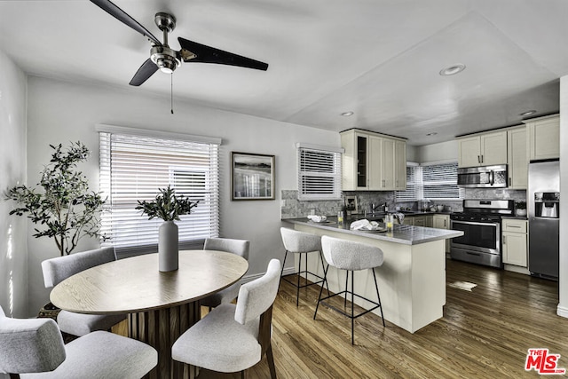 interior space with appliances with stainless steel finishes, dark hardwood / wood-style floors, tasteful backsplash, a breakfast bar area, and kitchen peninsula