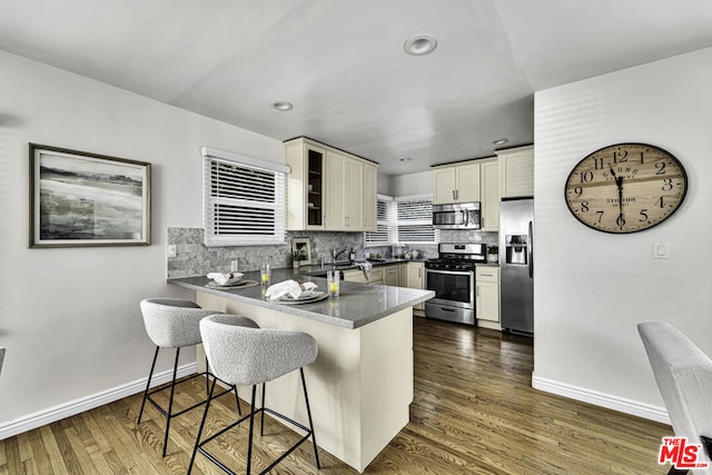 kitchen with appliances with stainless steel finishes, a breakfast bar area, dark hardwood / wood-style flooring, decorative backsplash, and kitchen peninsula