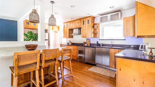 kitchen with wall chimney range hood, sink, hanging light fixtures, stainless steel appliances, and dark hardwood / wood-style flooring