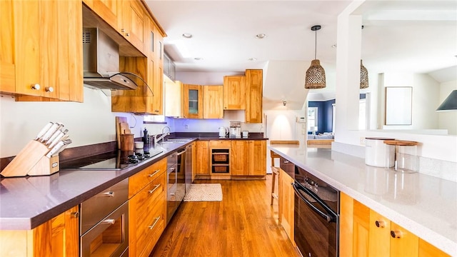 kitchen featuring wall chimney range hood, sink, black electric stovetop, light hardwood / wood-style floors, and decorative light fixtures