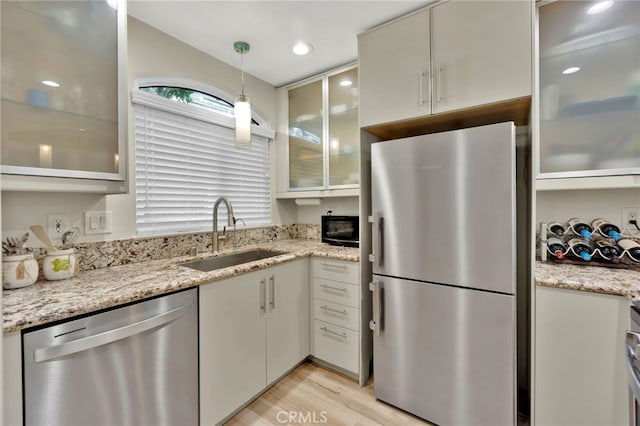 kitchen with sink, light hardwood / wood-style flooring, appliances with stainless steel finishes, pendant lighting, and light stone countertops