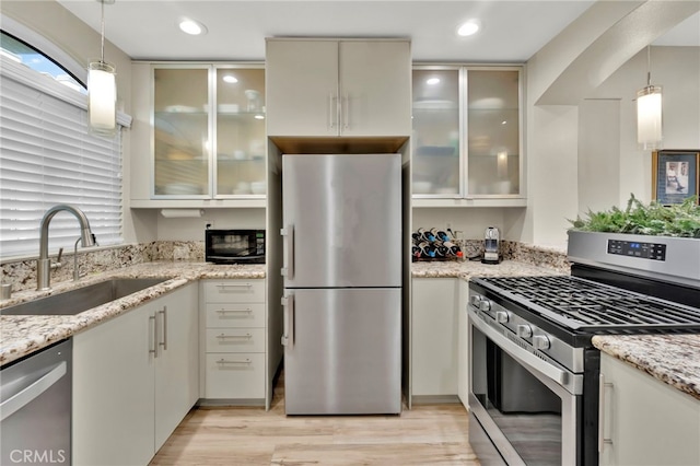 kitchen with light stone countertops, appliances with stainless steel finishes, sink, and pendant lighting