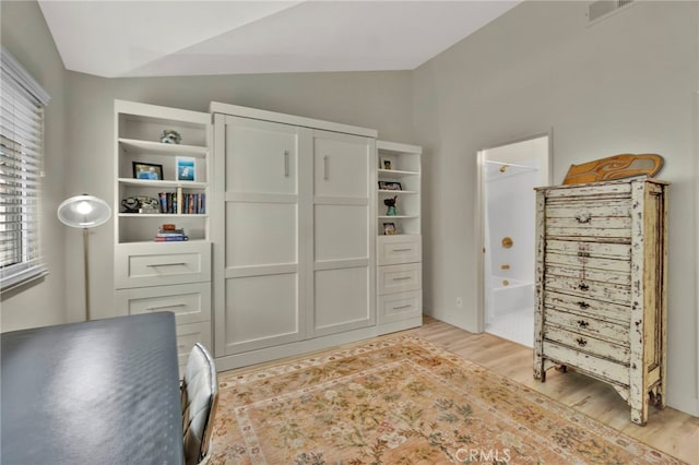 bedroom with lofted ceiling, connected bathroom, and light hardwood / wood-style floors