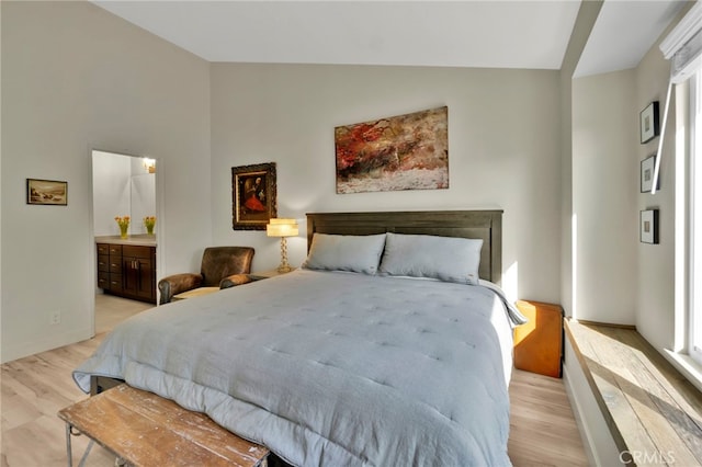 bedroom with vaulted ceiling, connected bathroom, and light hardwood / wood-style flooring