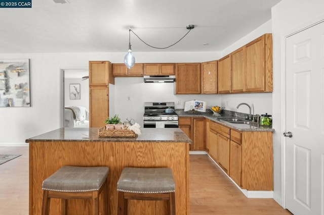 kitchen with sink, stainless steel gas range, a breakfast bar, hanging light fixtures, and light hardwood / wood-style floors