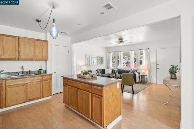 kitchen featuring sink, light hardwood / wood-style flooring, ceiling fan, stone counters, and a kitchen island