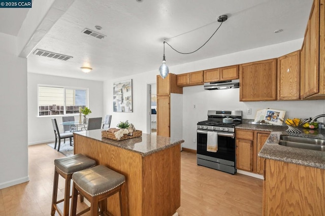 kitchen with gas stove, a kitchen island, sink, and light hardwood / wood-style floors