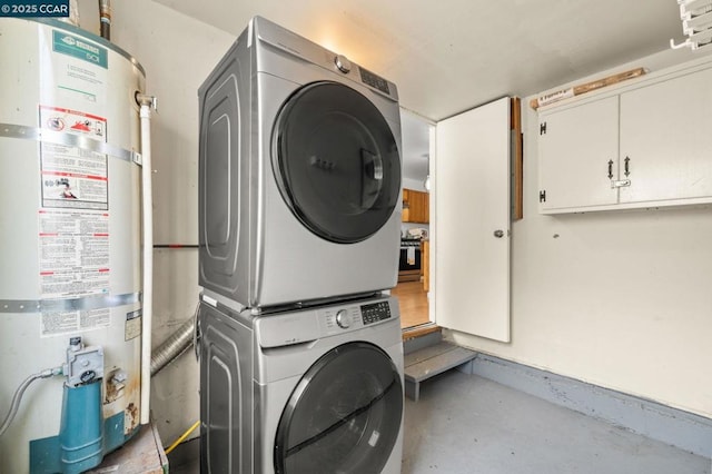 laundry area featuring water heater, stacked washer / dryer, and cabinets