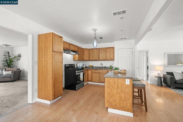 kitchen featuring stainless steel range with gas cooktop, a breakfast bar, pendant lighting, sink, and light wood-type flooring