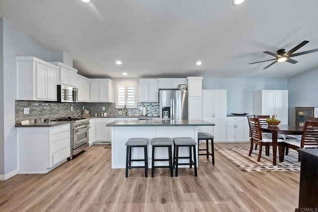 kitchen with a kitchen island, appliances with stainless steel finishes, a breakfast bar, white cabinetry, and backsplash