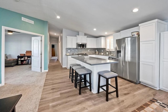 kitchen with sink, a breakfast bar area, stainless steel appliances, white cabinets, and a kitchen island