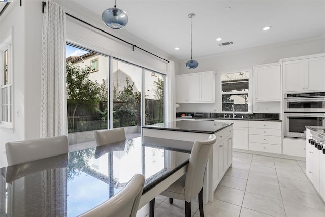 kitchen featuring light tile patterned flooring, decorative light fixtures, white cabinetry, sink, and stainless steel double oven