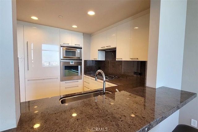 kitchen featuring appliances with stainless steel finishes, sink, dark stone countertops, white cabinets, and kitchen peninsula