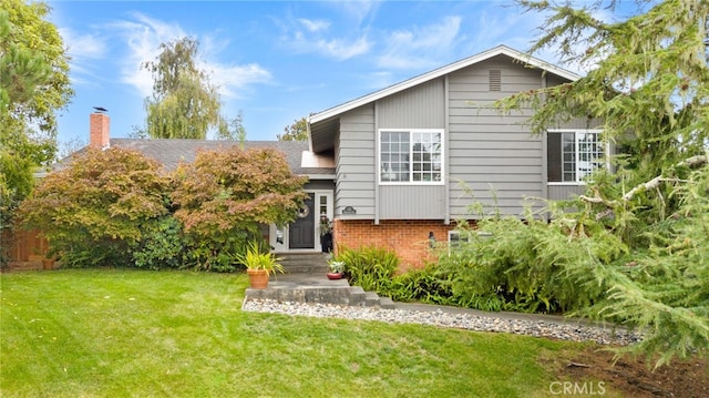 tri-level home featuring brick siding, roof with shingles, and a front yard