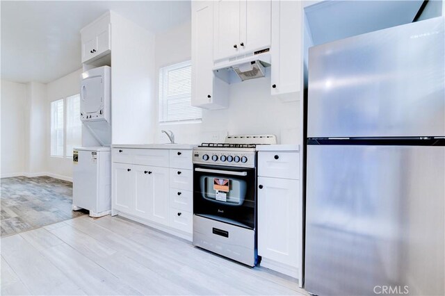 kitchen featuring light hardwood / wood-style flooring, stainless steel refrigerator, range, stacked washer / drying machine, and white cabinets