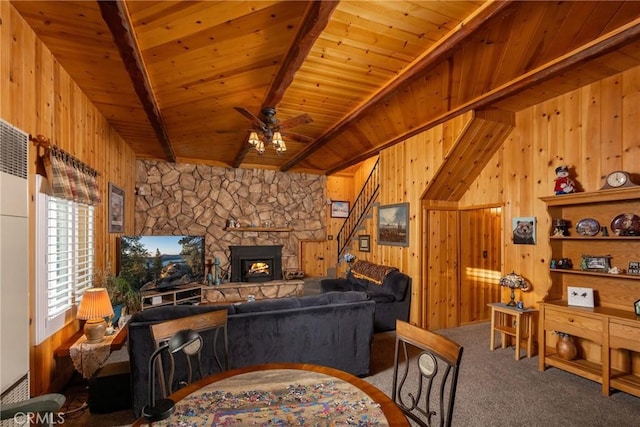 carpeted living room featuring wood ceiling, ceiling fan, a stone fireplace, beamed ceiling, and wood walls