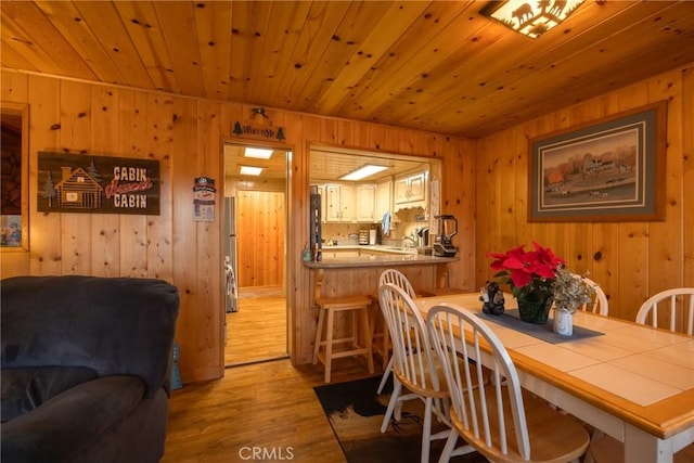 dining room with sink, wood ceiling, wooden walls, and light hardwood / wood-style floors