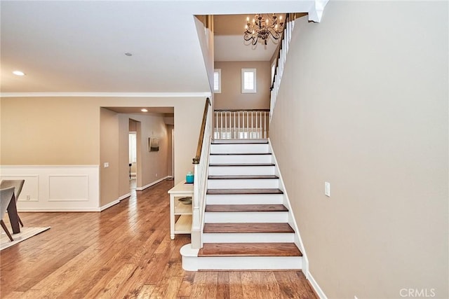 staircase with hardwood / wood-style flooring, crown molding, and a chandelier