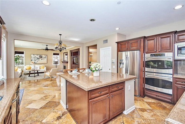 kitchen with a kitchen island, light stone countertops, appliances with stainless steel finishes, and pendant lighting