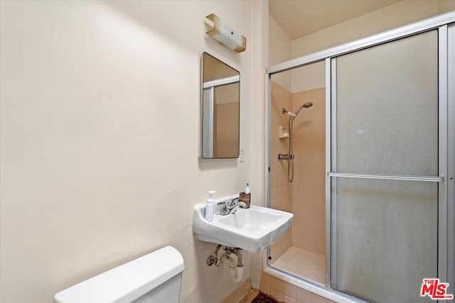 bathroom featuring toilet, a shower with shower door, and sink